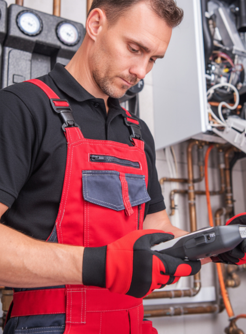 Techniker liest im modernen Badezimmer ein Lesegerät aus, während im Vordergrund ein roter Werkzeugkoffer den Wartungsservice von Rechtenbach-Buttron symbolisiert.